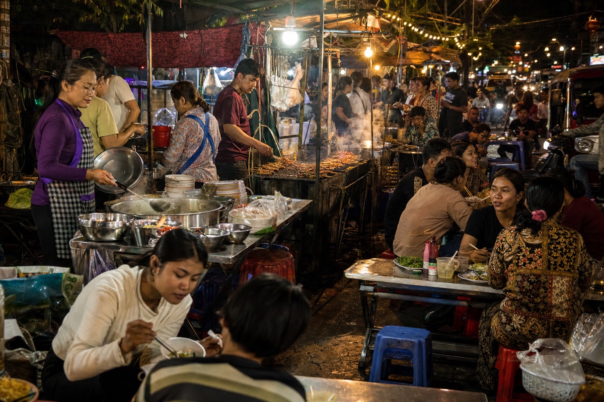 A lively Cambodian street food market in the evening, vendors and diners at low tables under string lights