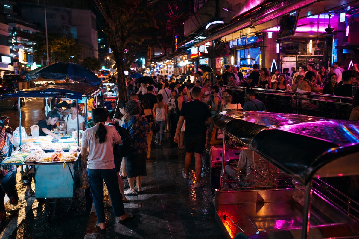 A neon-lit Bangkok nightlife street in the evening, bar signs glowing over a busy sidewalk crowd