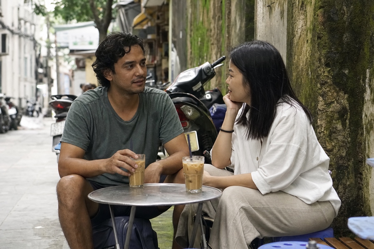 A foreign man and a Vietnamese woman on low stools with Vietnamese iced coffee on a Hanoi street